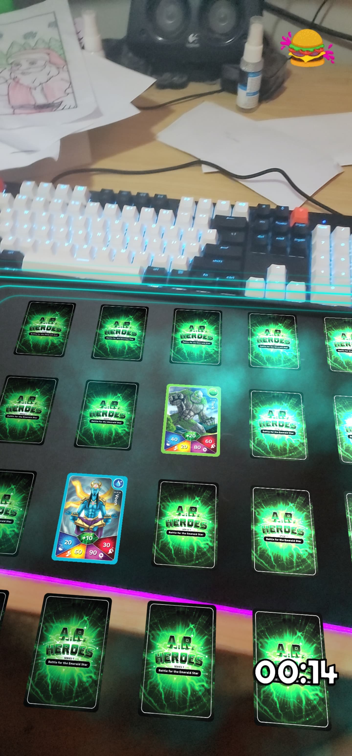 Screenshot of the AR Heroes branded version of the Memory Card game in AR. The players desk and keyboard can be seen in the frame. One pair of cards are flipped, but do not match. There is a timer on the screen showing 14 seconds have passed