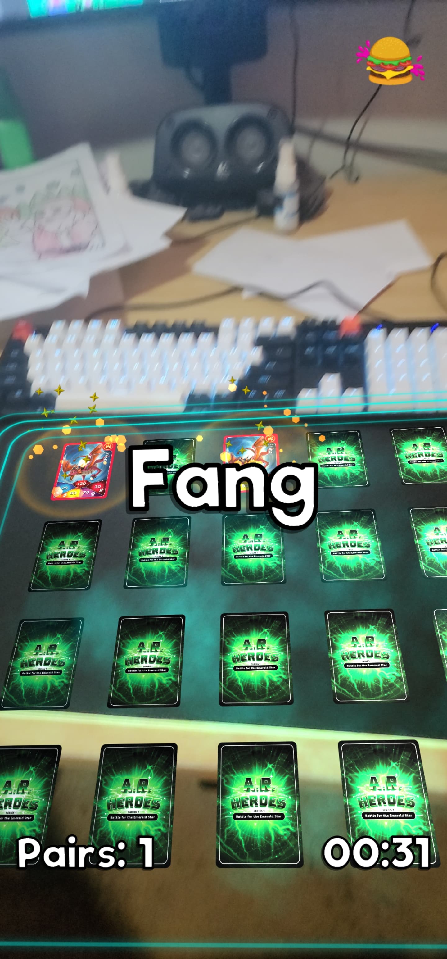 Screenshot of the AR Heroes branded version of the Memory Card game in AR. The players desk and keyboard can be seen in the frame. A matched pair of cards are flipped with some sparkling effects shown. A text pop up saying 'Fang' is displayed in the middle of the screen indicating Fang is the matched card. There is a timer on the screen showing 31 seconds have passed. There is a text element stating there is one pair matched